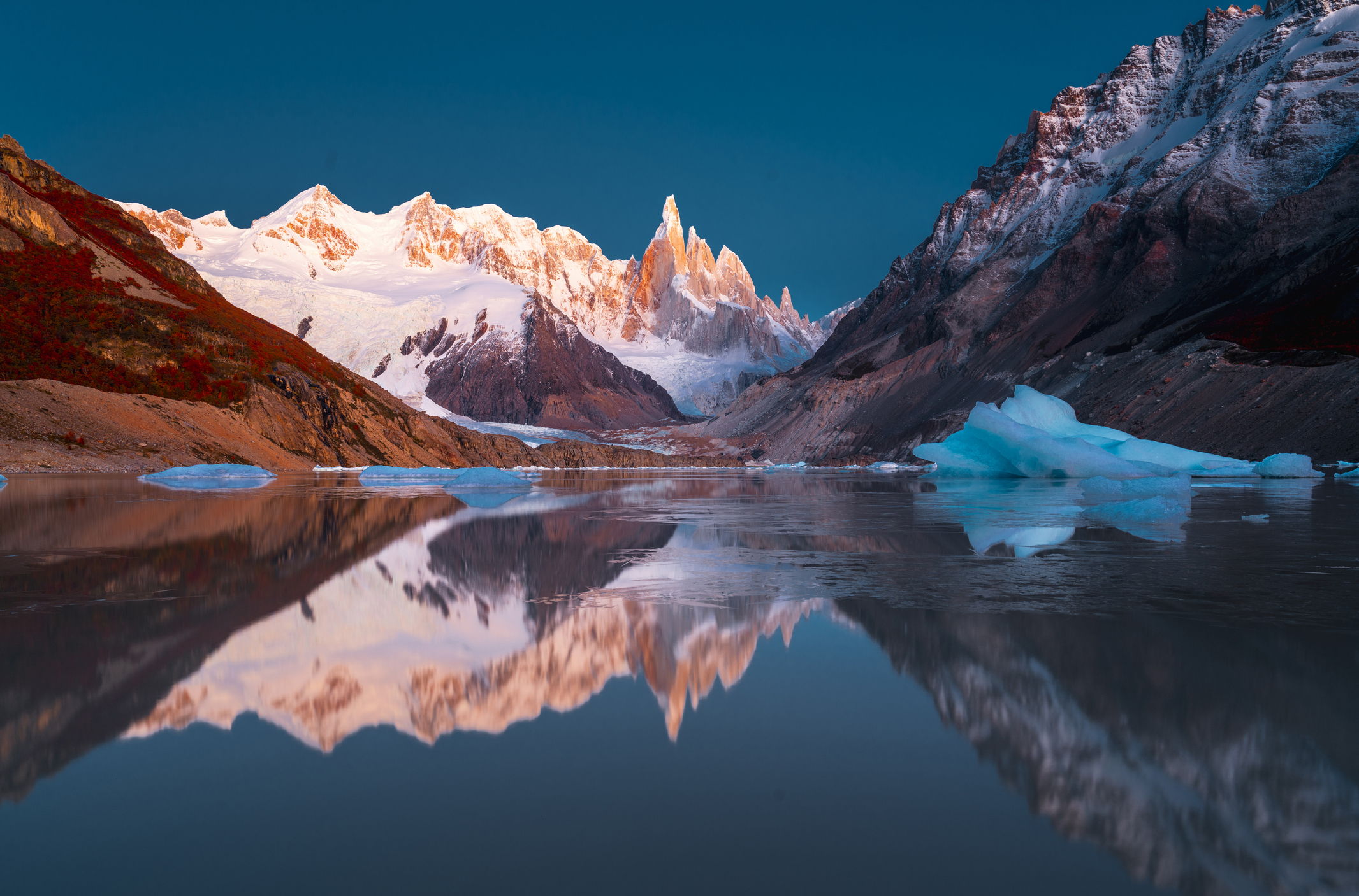 Snowy mountains in sunlight reflecting in an icy lake