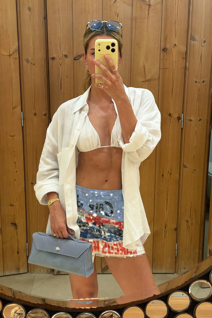 a woman wearing a bikini top, sequin skirt, and white button-down