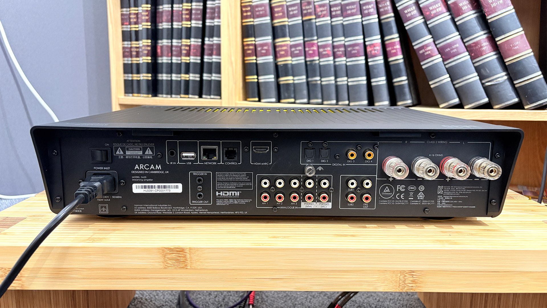 Arcam SA35 music streamer on wooden hi-fi rack in front of bookcase showing rear of unit