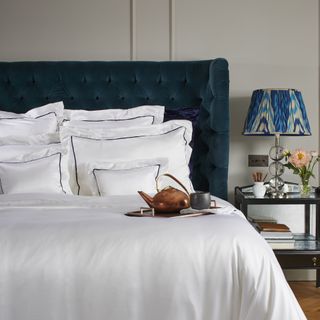 white silk sheets and pillowcases with border on bed with velvet headboard