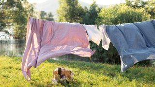 Pink, blue and white bedding being on a clothesline outside on a bright sunny day