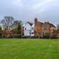 Large green grass lawn in front of row of espalier trees and house in winter garden