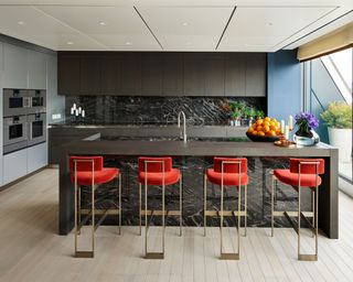 Modern grey kitchen with handleless cabinets and red bar stools.
