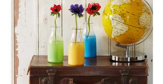 three colourful vases with flowers on top of a brown leather suitcase next to a yellow world globe