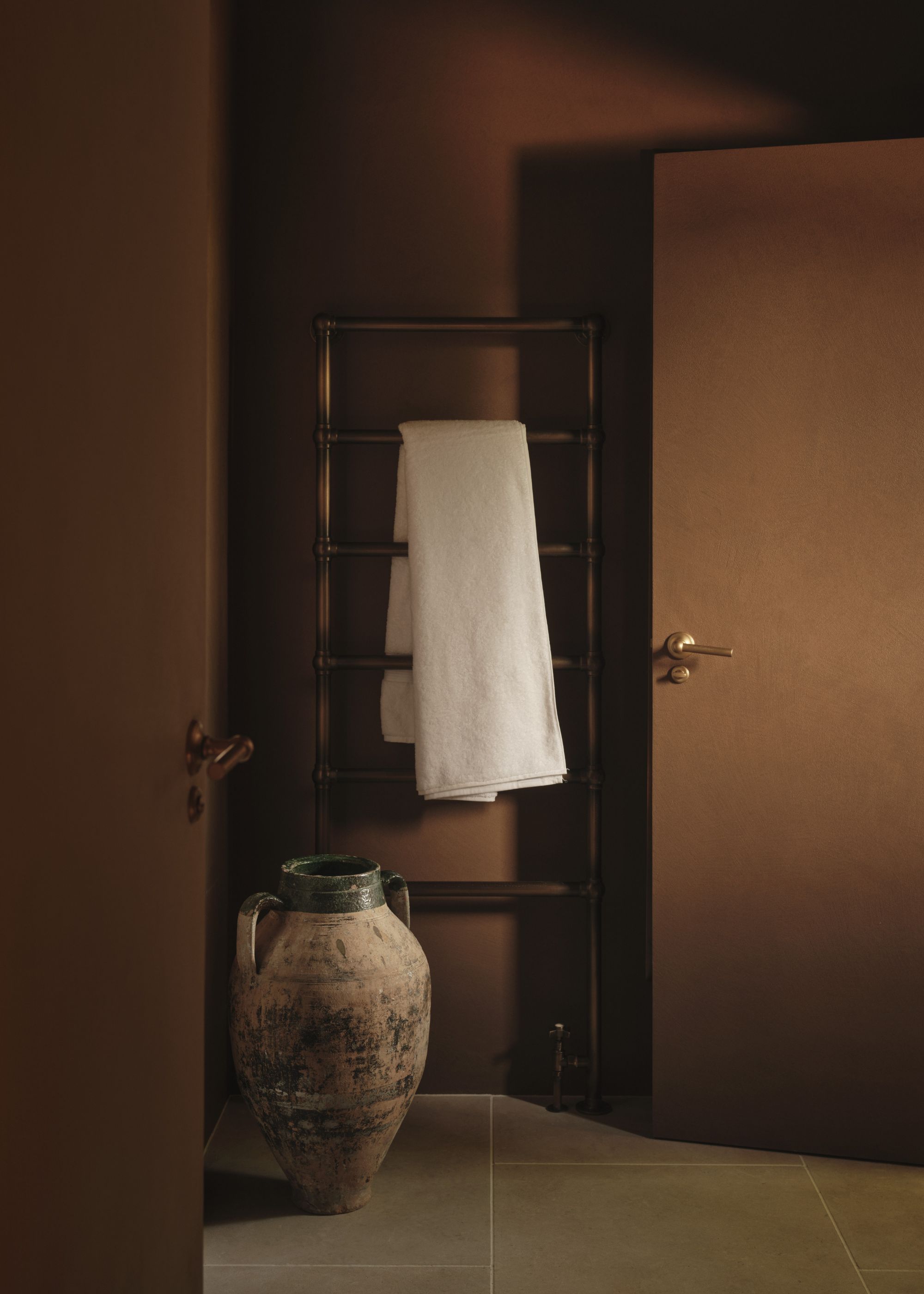 A bathroom with a towel holder and a towel hanging on the towel rack. A pot is also placed beside the door and towel rail