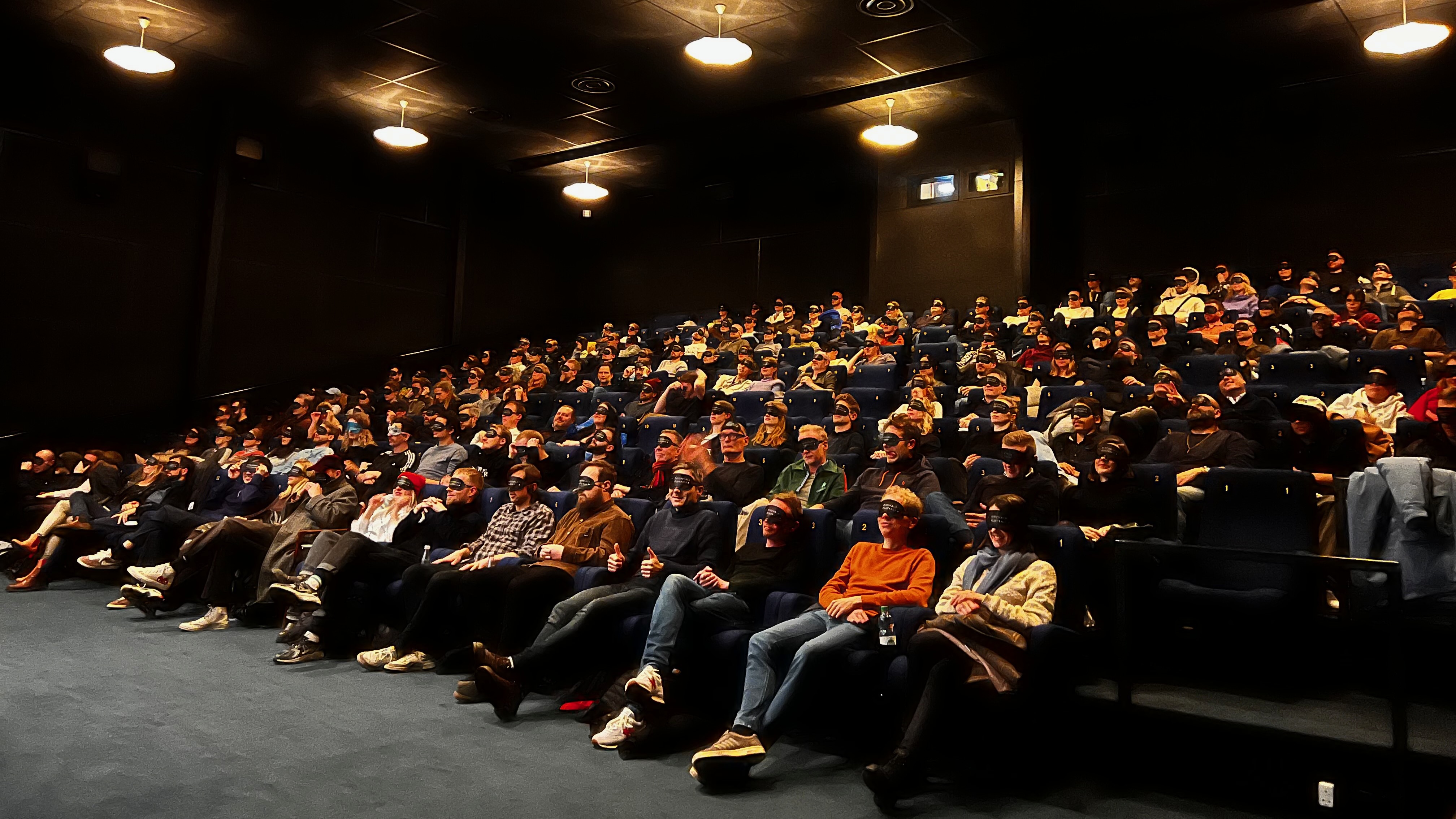 A crowd in a cinema, all wearing Pitchblack Playback eye masks.