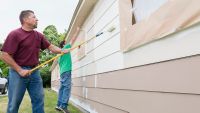 Two men painting the exterior of a house white with roller brushes