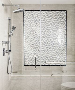 A shower with grey and white marble chevron tiling