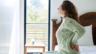 Woman in jumper sitting on soft mattress with lower back pain