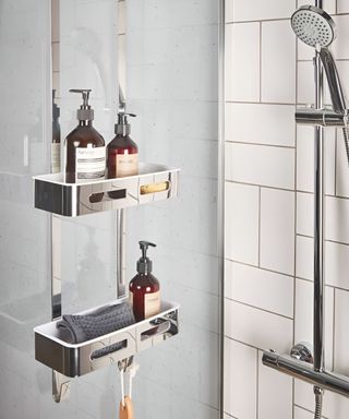 A white shower with a silver shower caddy, white tiles, and a silver shower head