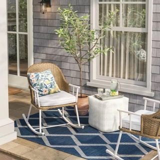 An outdoor patio setup on top of a large blue and white area rug, with a white ottoman