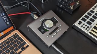 A Universal Audio Apollo Twin X audio interface on a desk with a MacBook, MIDI keyboard, and looper pedal