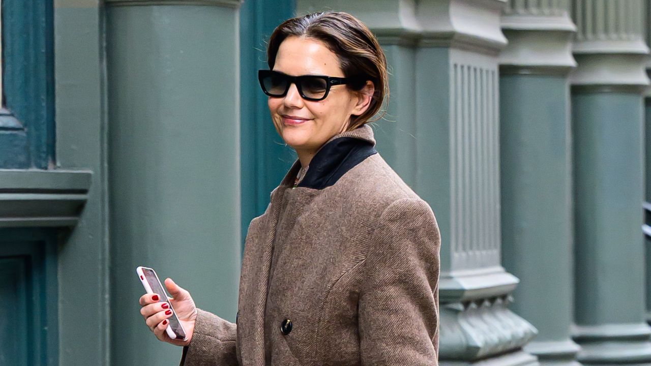 Katie Holmes walking in New York City wearing a longline coat with a belted bag and jeans