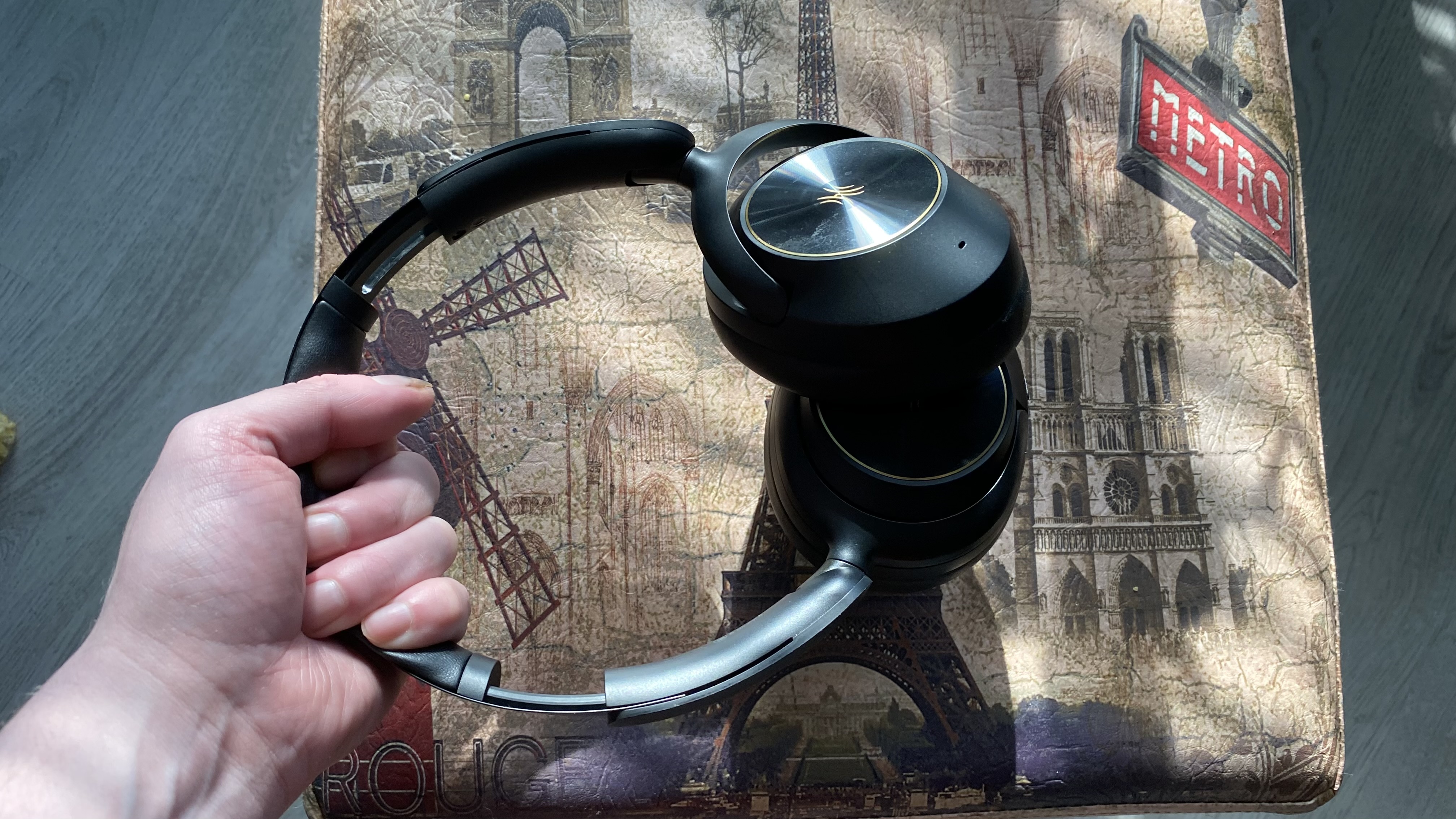 OneOdio Focus A6 over-ear headphones held by the headstrap over a Parisian stool