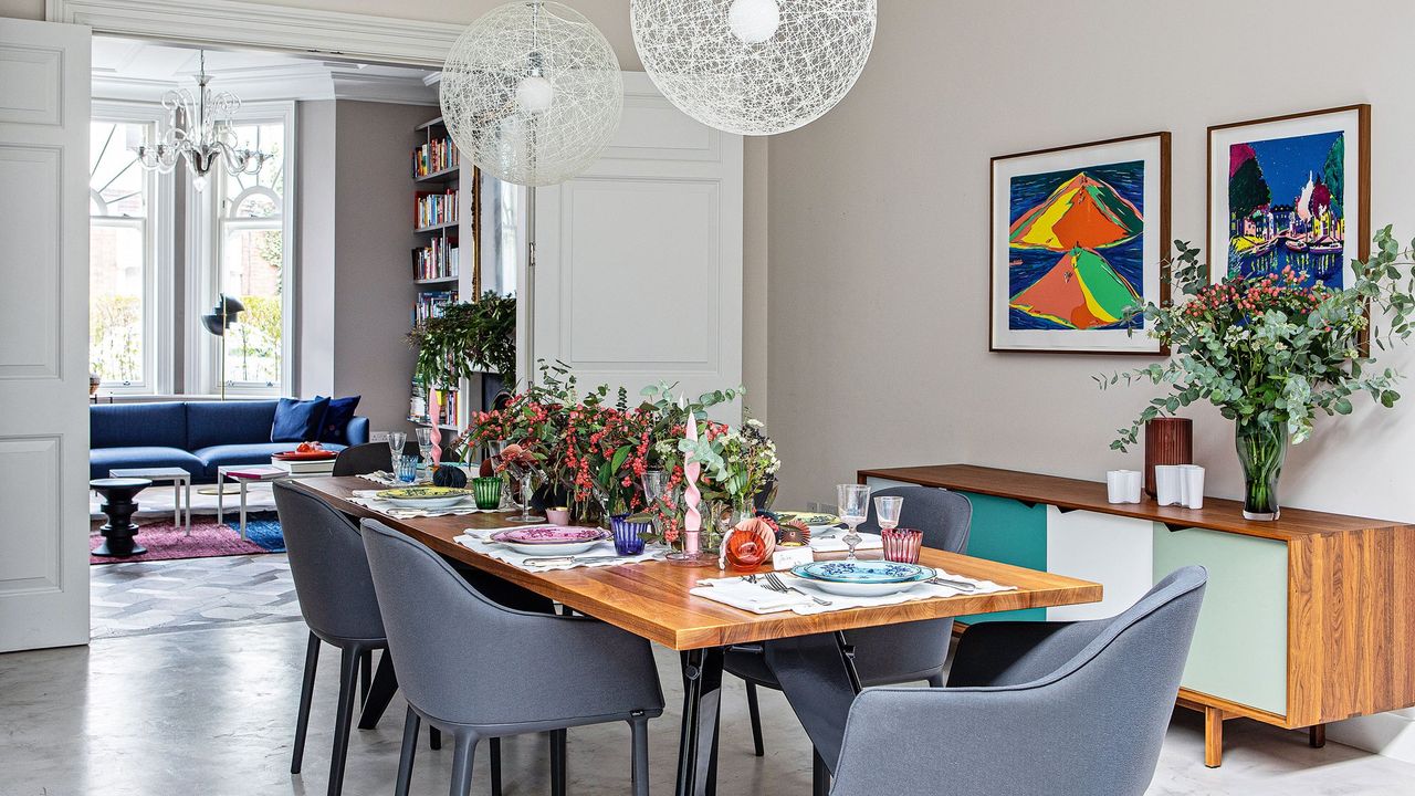 Dining room area with a wooden dining room table decorated with flowers and cutlery, with white modern lights hanging above the table