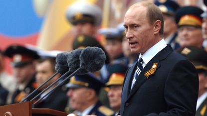 President Vladimir Putin speaking at a set of microphones wearing a Russian Victory Day Ribbon