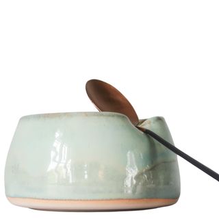 A green ceramic teabag holder with bronze spoon