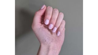 A close up of Digital Beauty Writer, Naomi Jamieson's hand with milky-pink short nails, pictured in front of a dark green wall