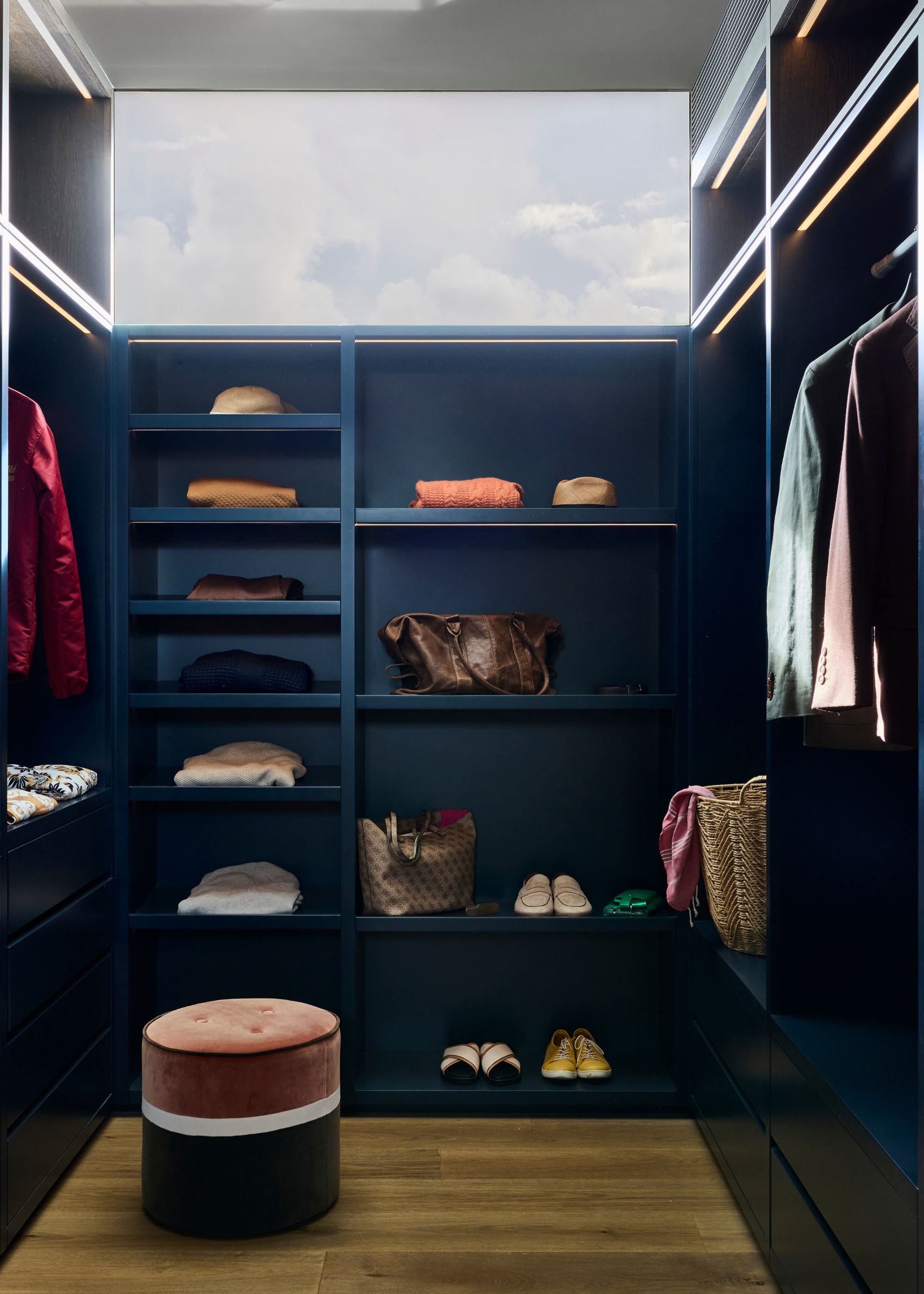 A blue wardrobe with open shelving, a colorful pouffe, and clothes