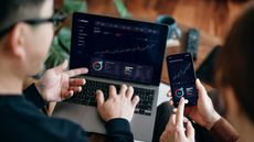 Two investors look at an investing graph showing a line going up on a laptop screen.