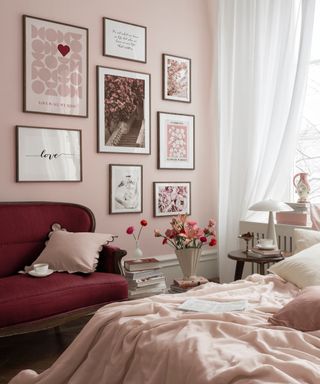 A pink bedroom with a gallery wall of artworks, a purple couch, and a pink bed