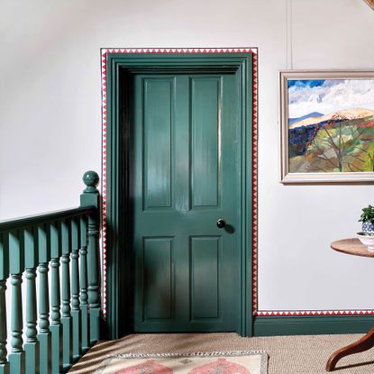 hallway with white walls and green doors and banister with red and white geometric border around the door and skirting border with natural carpet and artwork on the wall