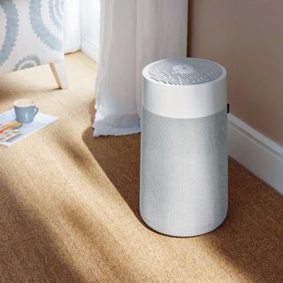 White air purifier on natural flooring with white curtain behind