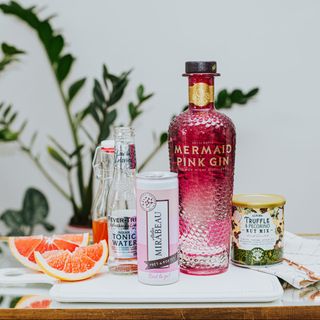 Mermaid Pink Gin on a board with a selection of tonics. mixers and snacks