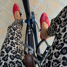 Anne wears leopard pants with red ballet pumps while riding a bike.