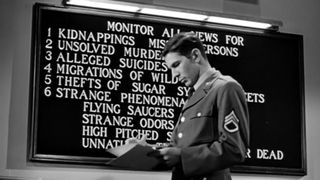 A man in military uniform stands in front of a blackboard that writing on it