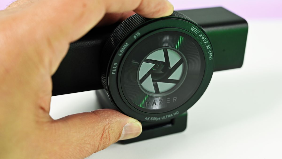 A hand adjusting the integrated mechanical privacy shutter on the front lens ring of the Razer Kiyo V2 Pro webcam.