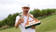 Camilo Villegas looks at his phone whilst holding the Bermuda Championship trophy