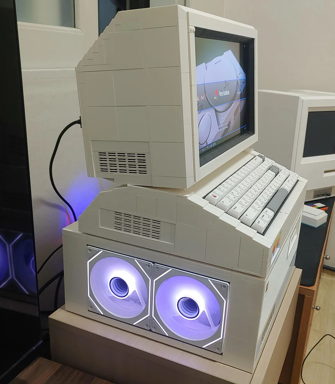 Retro-style computer made from LEGO bricks, featuring a modern monitor with a red swirl design on the screen. Includes front fan lights and rainbow detail.