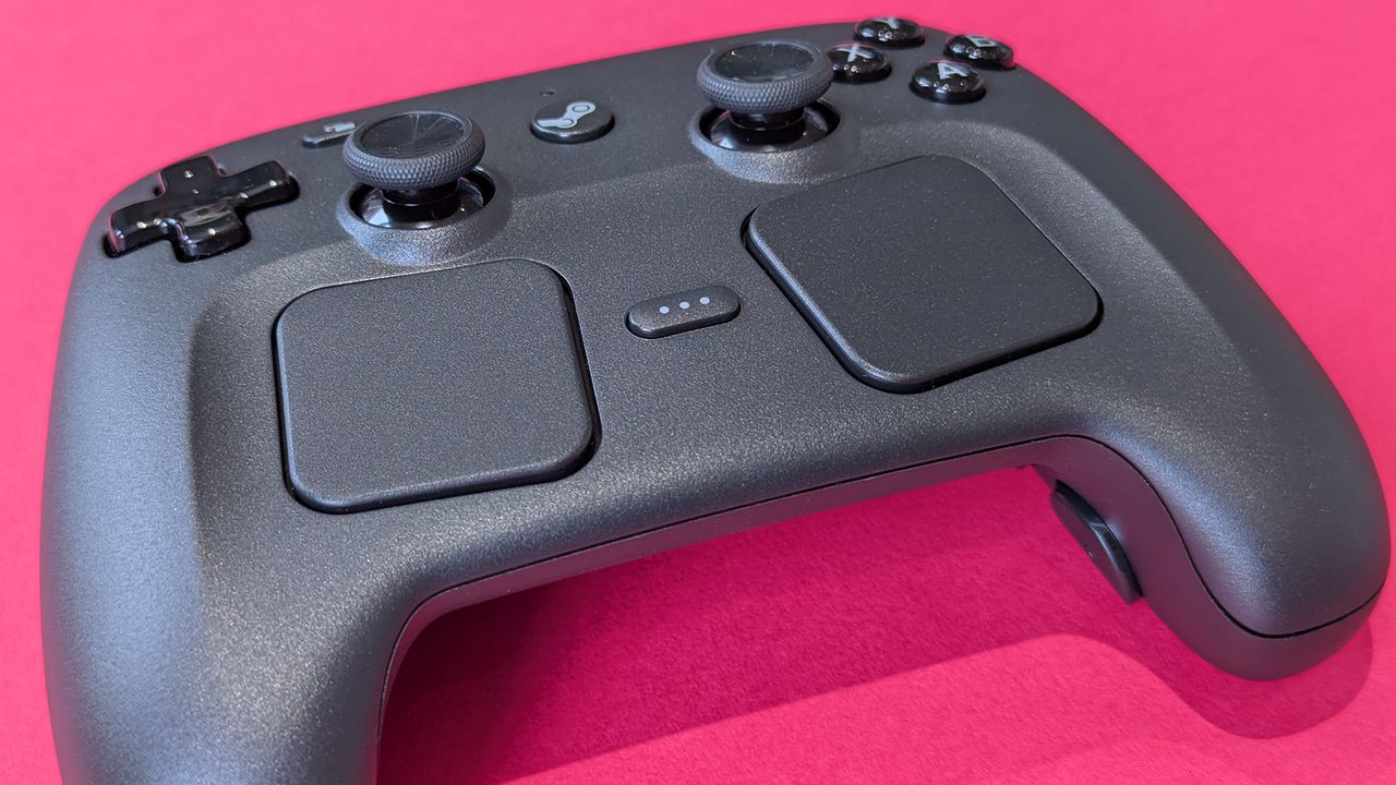 Close-up shot of the Valve Steam Controller (2026), highlighting its trackpads, displayed against a magenta card background