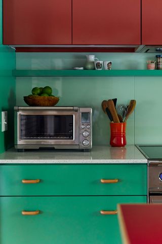 kitchen with red wall cabinets white worktop green base units and steel microwave with red utensil jar