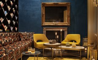 Seating area, 2 mustard yellow chairs, patterned couch with side tables, large mirror above fireplace