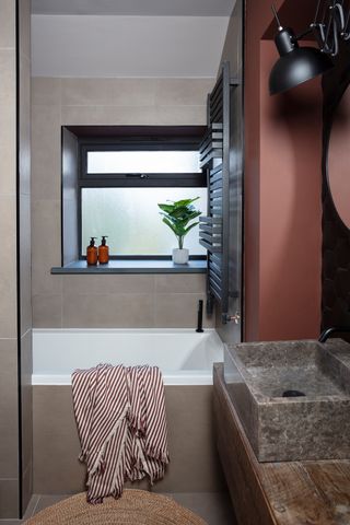 Small bathroom with brown wall tiles, burgundy painted walls and stone basin