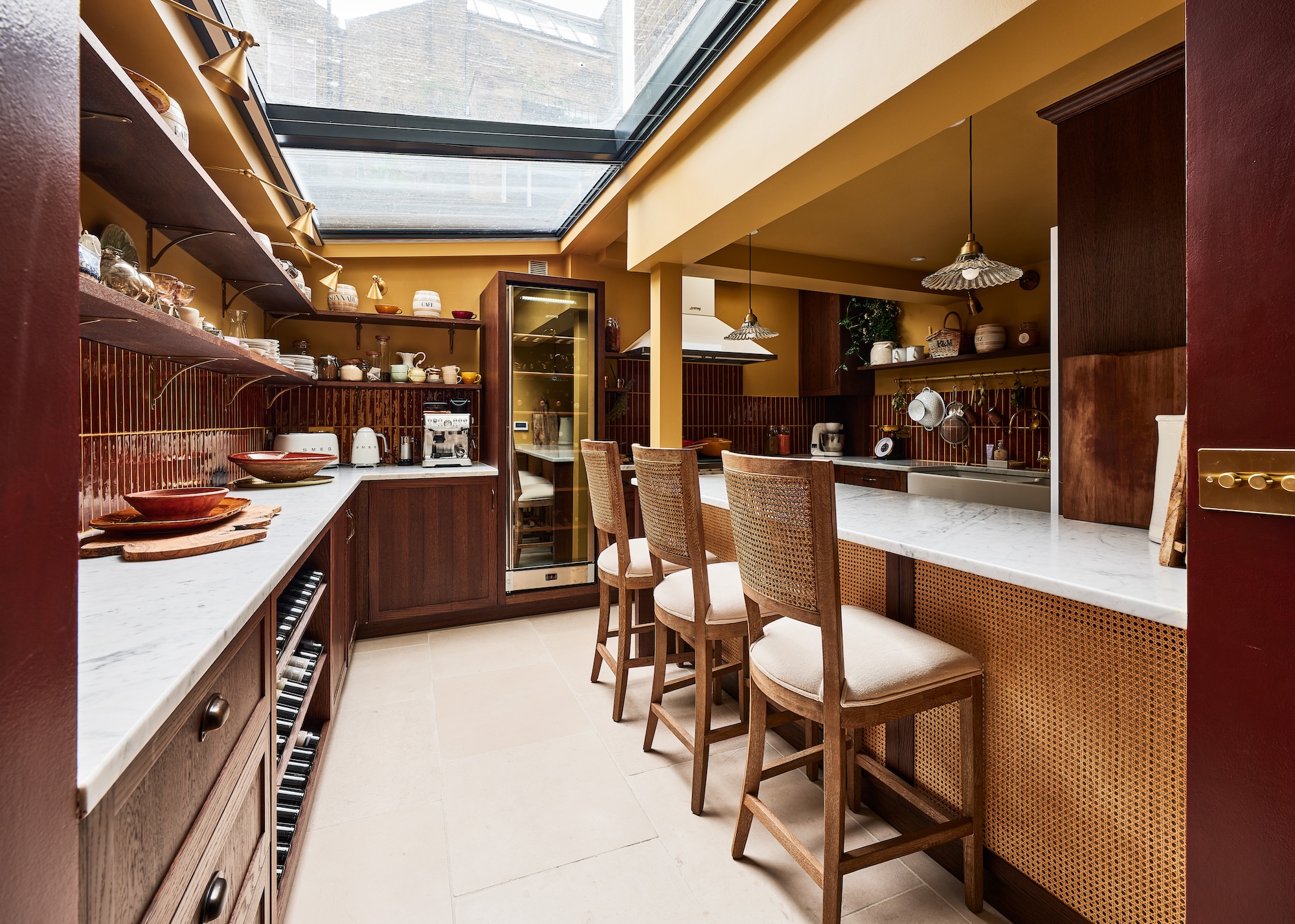A chefs kitchen with a bar seating area and bar stool beside it. There is also countertop space with kitchen accessories on top of it as well as open shelving with additional storage space
