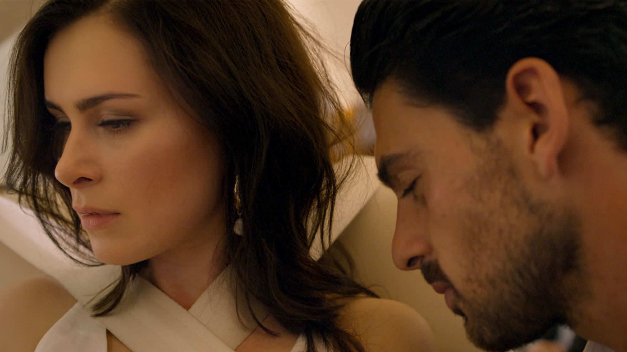 A man with his eyes closed leaning into a woman with dark hair, who is looking away