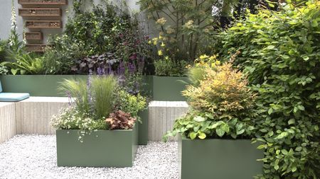 Plants growing in green containers and raised beds surround a seating area and gravelled patio area at the Chelsea Flower Show