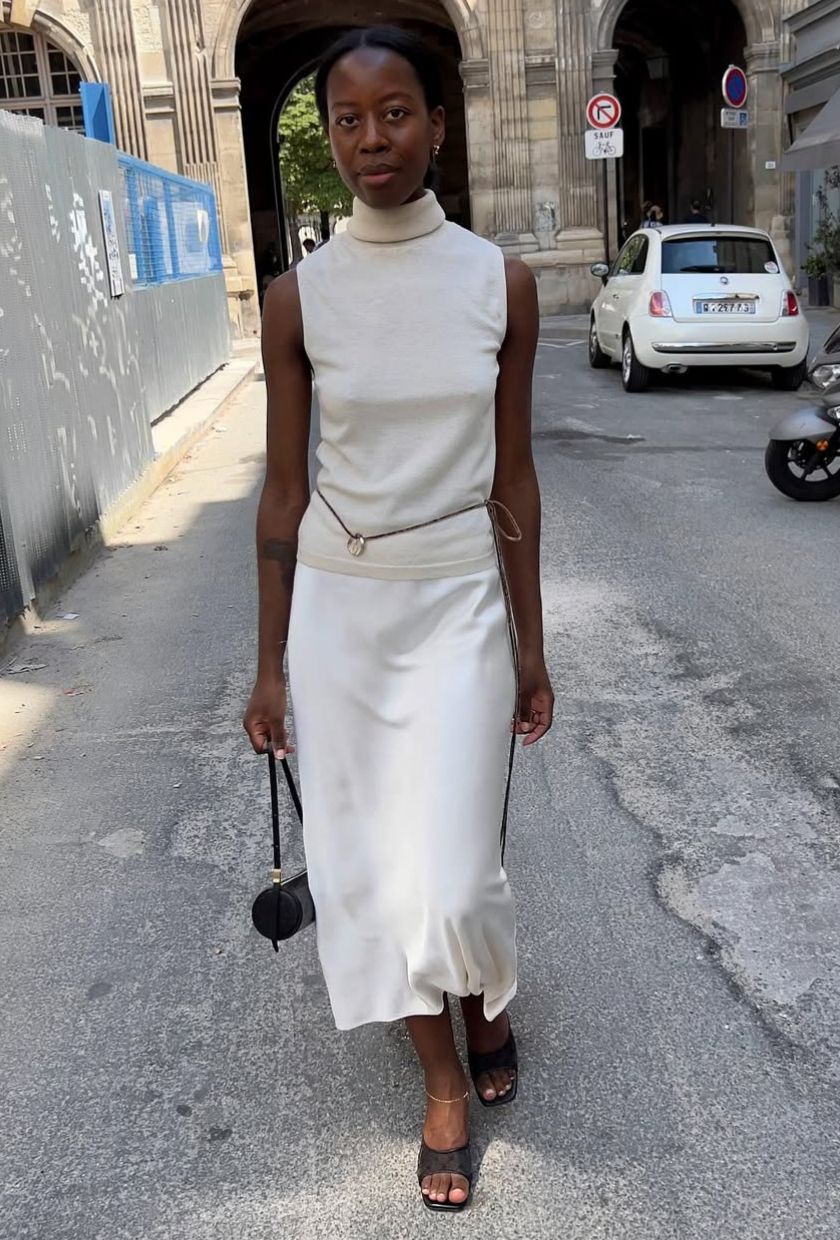 @sylviemus wears a high-neck top, cream slip skirt, black heels and a black barrel bag