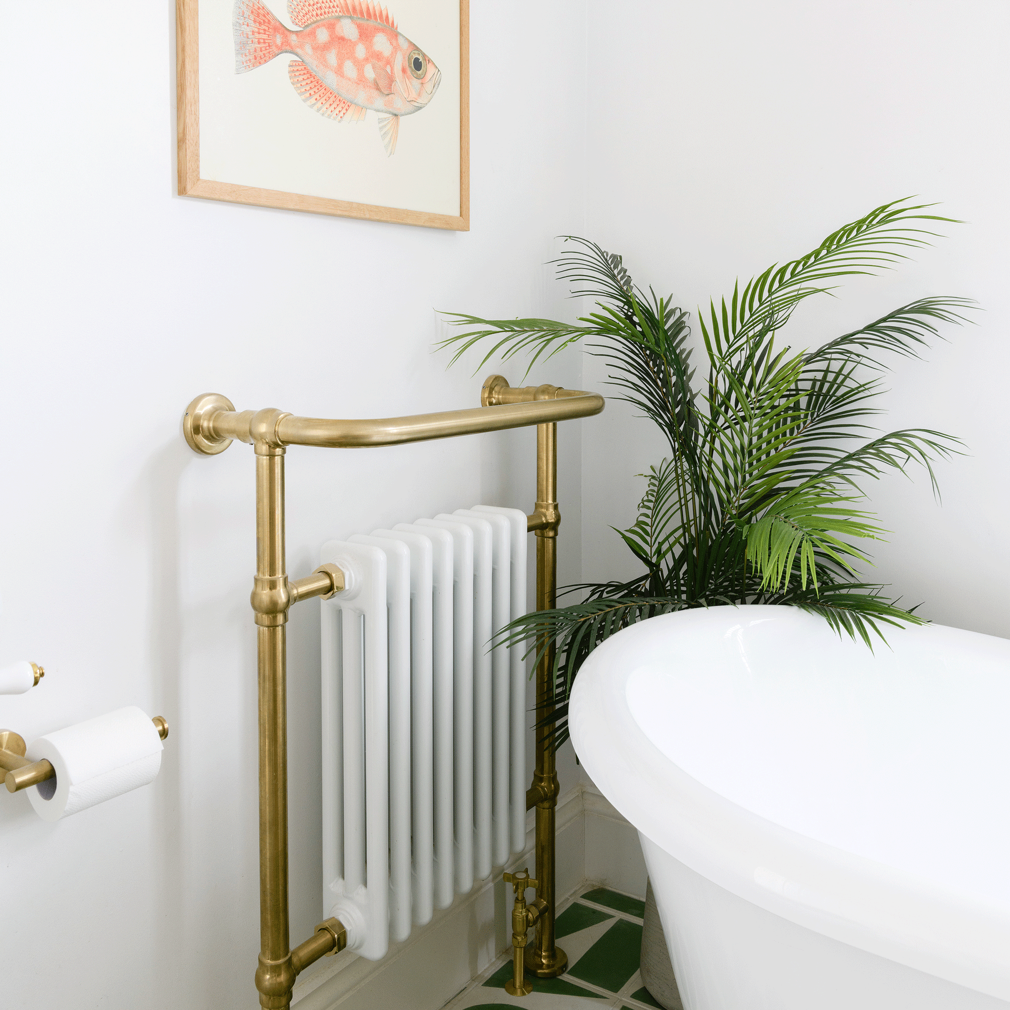 a white bathroom with traditional radiator with a brass towel rail beside a freestanding bath