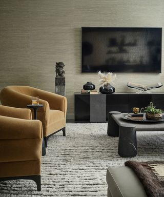 A moody living room with a lush rug and velvet armchairs