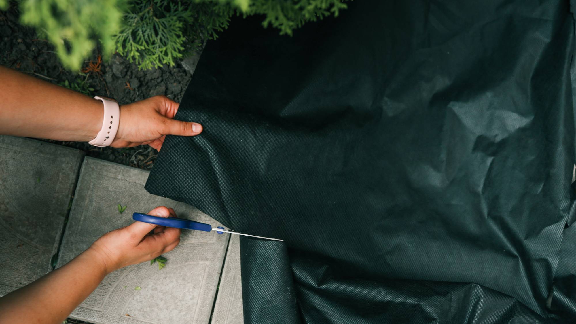 Hands using scissors to cut black landscape fabric