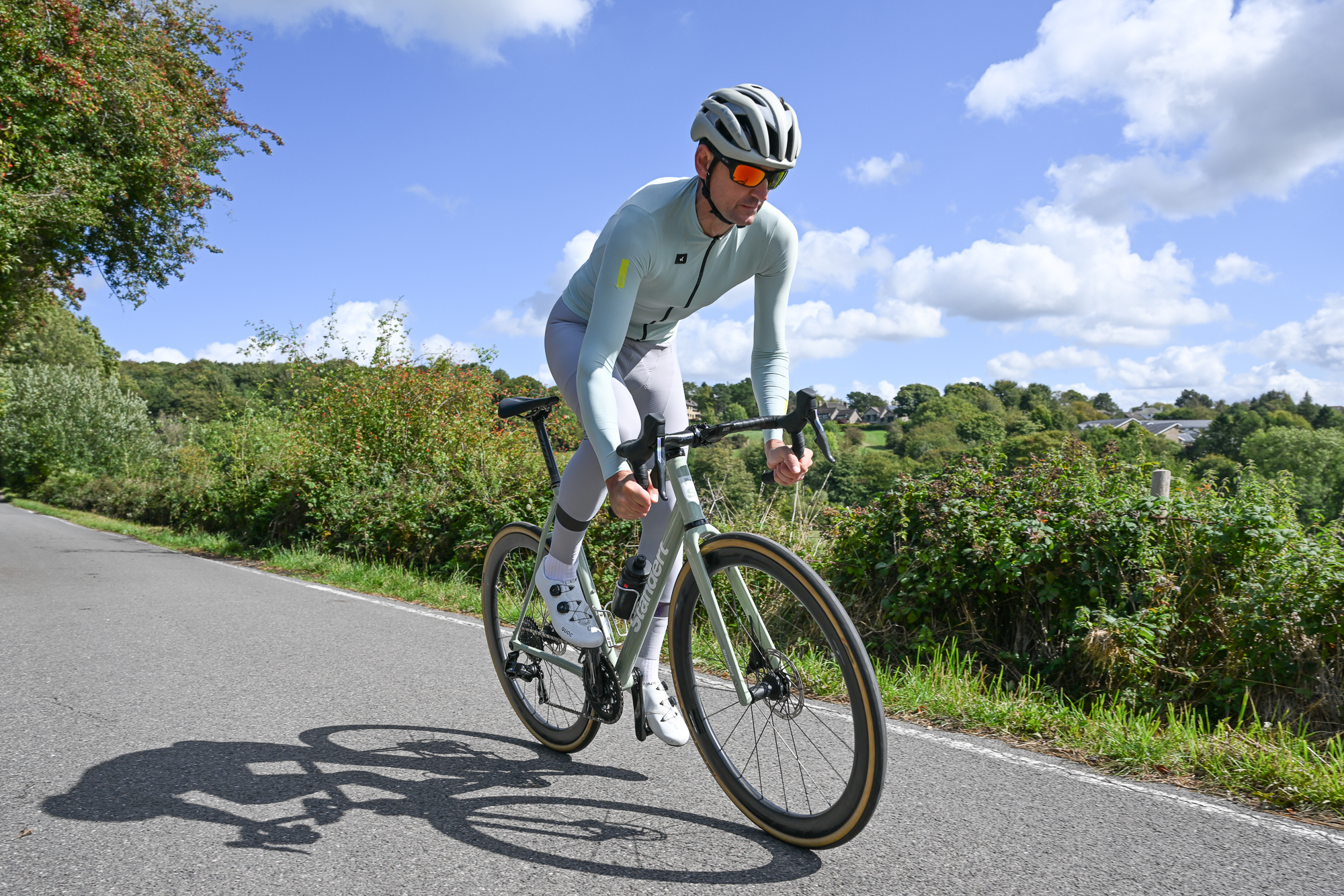 Man riding a green Standert Pfadfinder down a lane out of the saddle wearing a green jersey, grey tights and a beige helmet