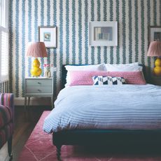 A bedroom with a botanical-style striped wallpaper, horizontally striped bedding and and a striped chair on the side