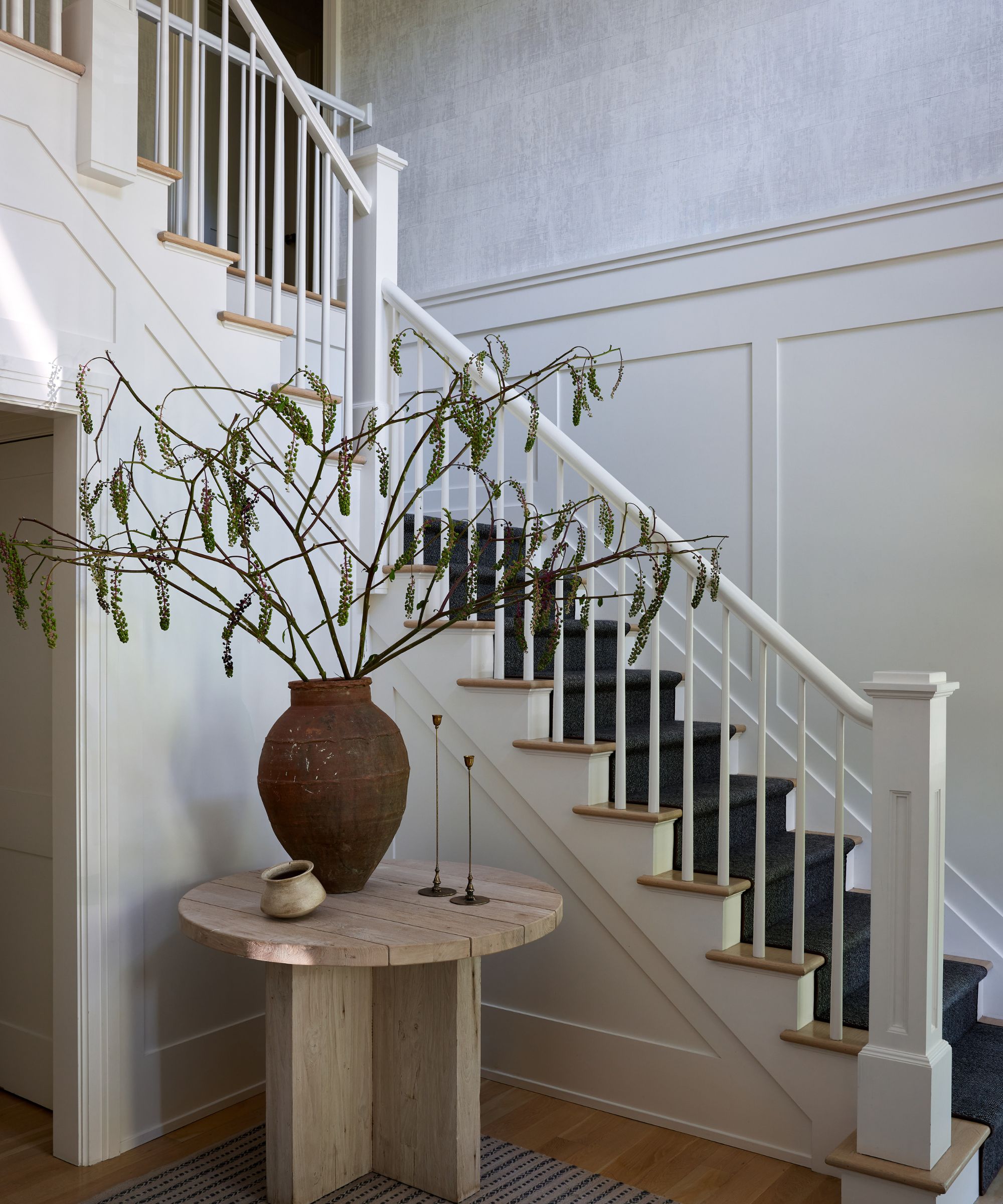 Entryway with wooden round table with rustic vases and staircase painted white