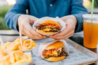 A person holding a cheeseburger along with fries.