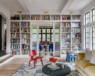 living room with built-in library wall, yellow sofa and bright red accent chair