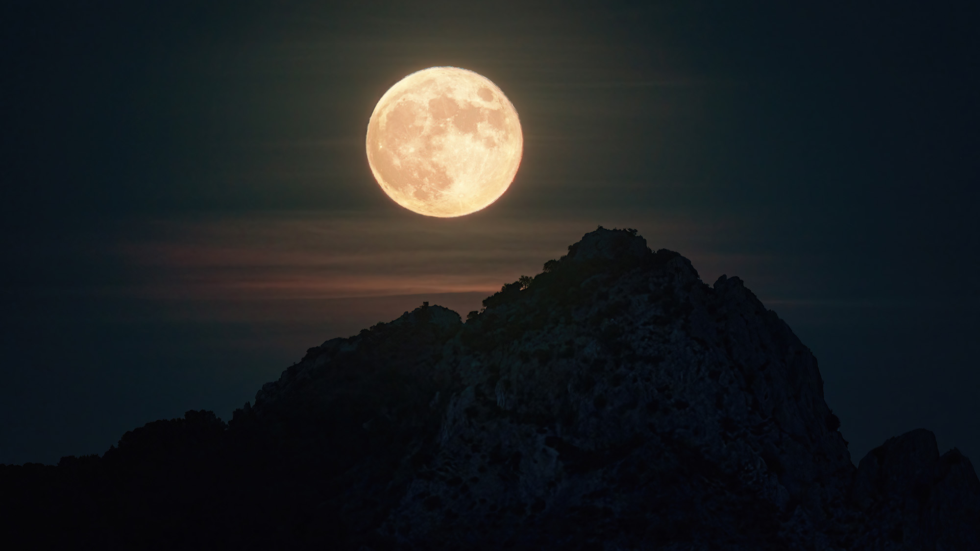 A large golden full moon is seen above a silhouetted peak